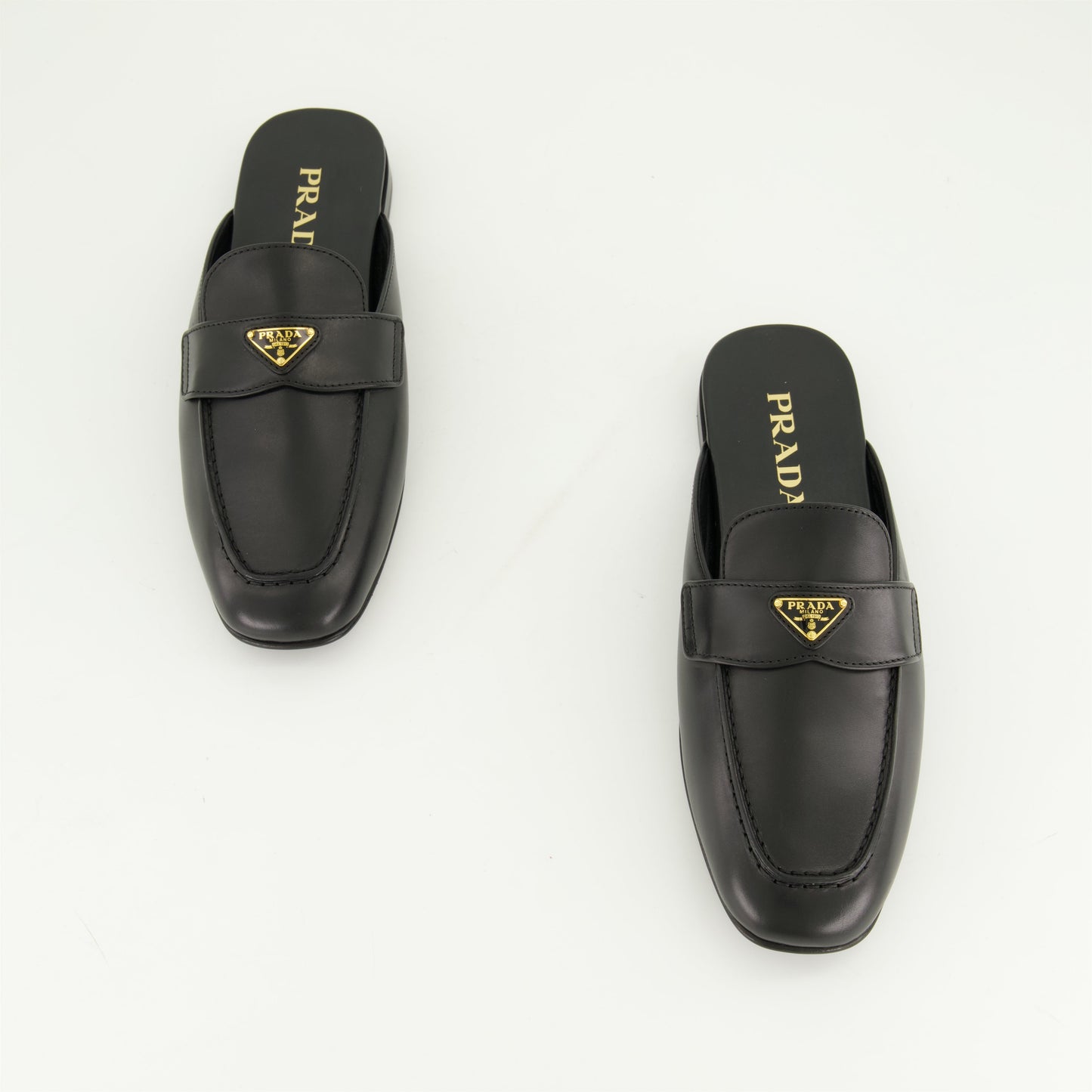 black leather mules, slip-on mules, metal logo mules, amande-shaped toe footwear, monobloc sole shoes