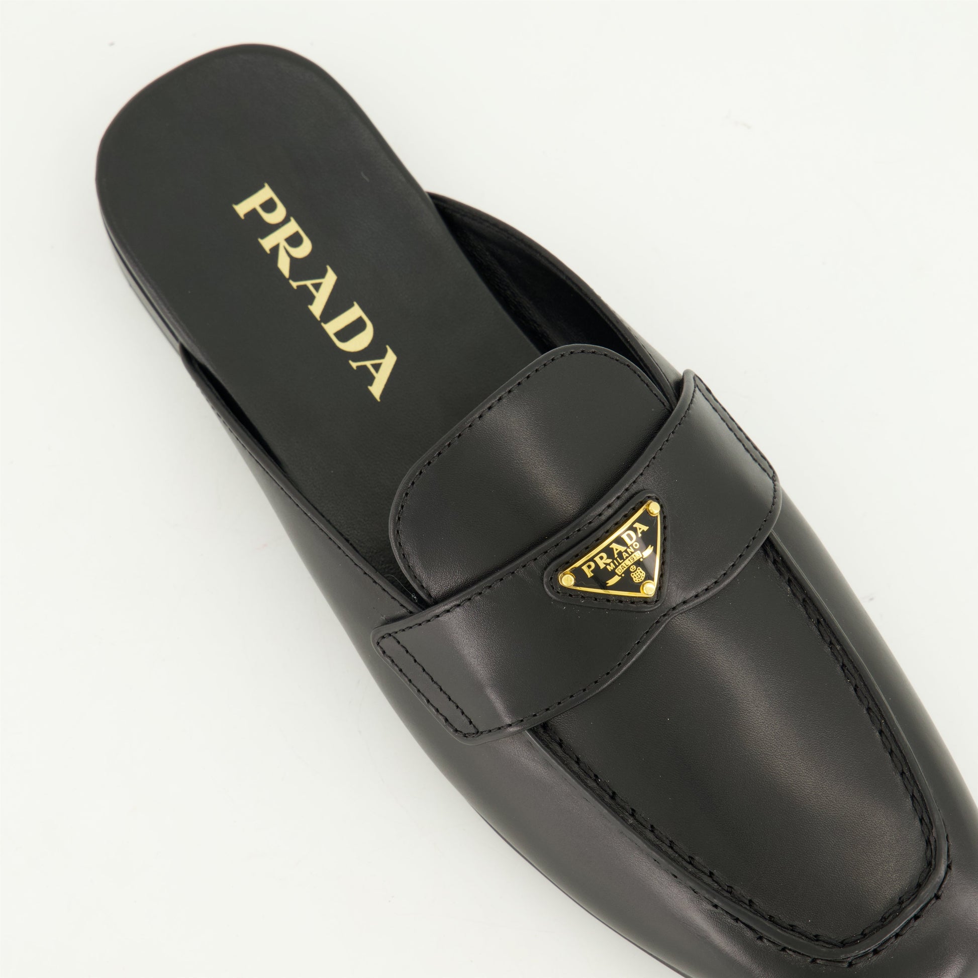 black leather mules, slip-on mules, metal logo mules, amande-shaped toe footwear, monobloc sole shoes